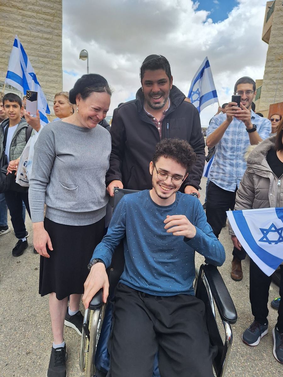 חנניה בכיסא גלגלים בין אנשים עם דגלי ישראל
